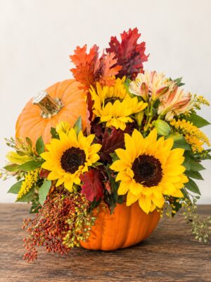 Fall flower pumpkin arrangement with yellow flowers, orange fall foliage, burgundy leaves, and cascading berries.