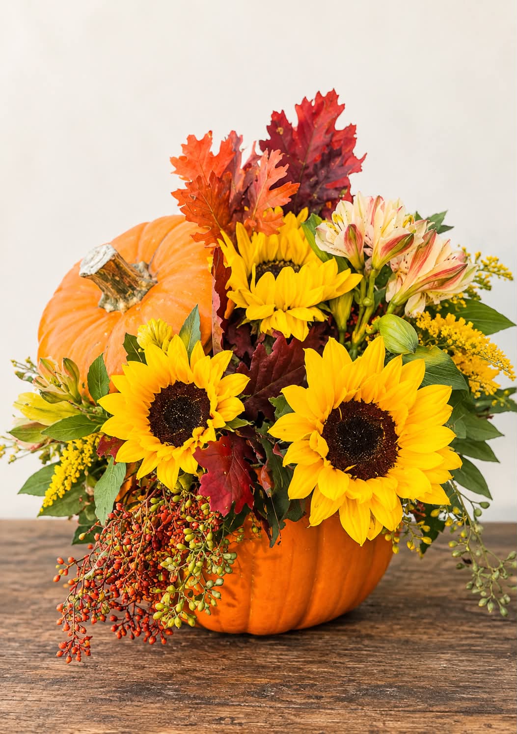 Fall flower pumpkin arrangement with yellow flowers, orange fall foliage, burgundy leaves, and cascading berries.