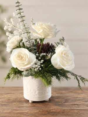 White rose and evergreen Christmas arrangement with frosted winter accents in a cream ceramic vase