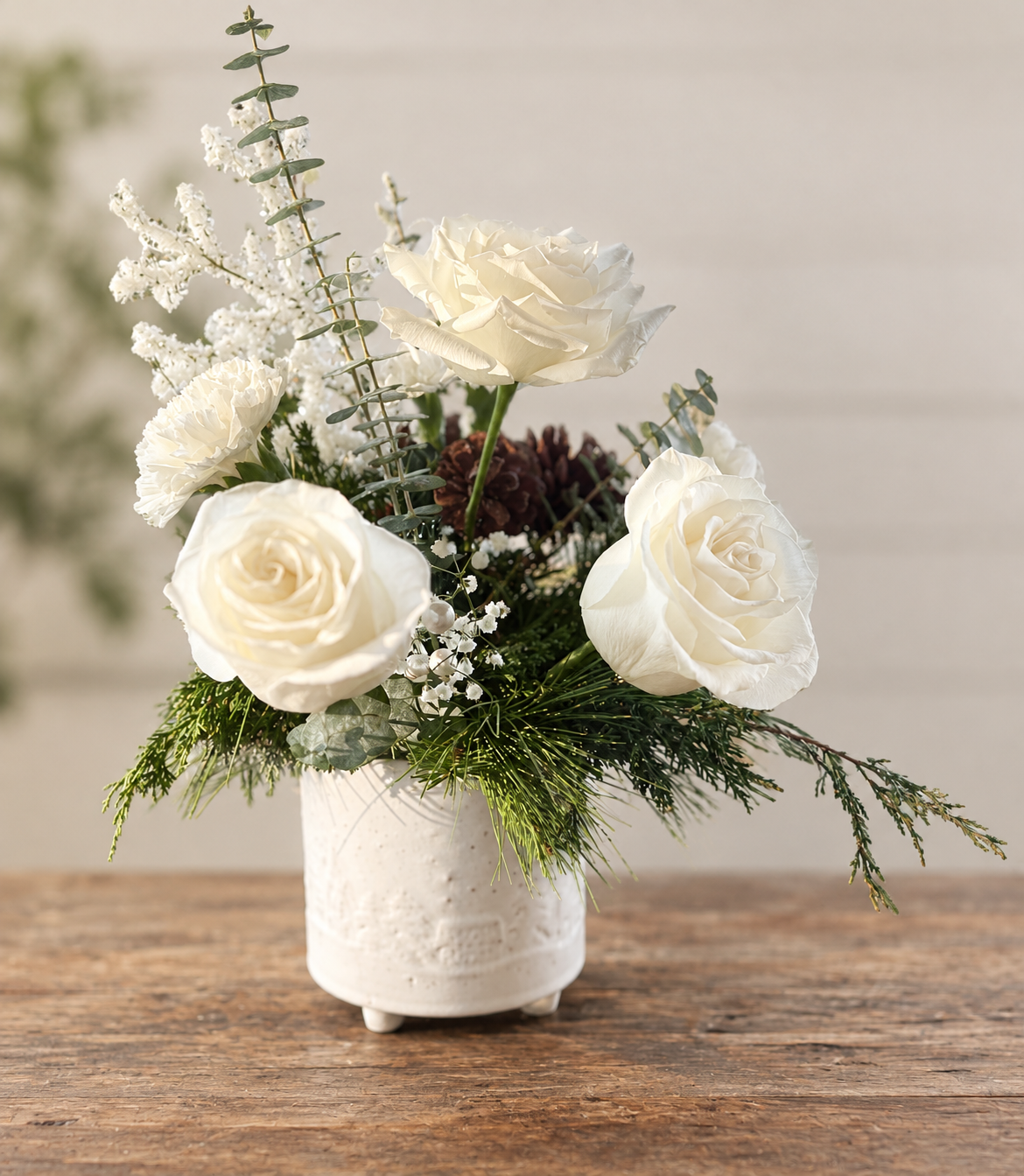 White rose and evergreen Christmas arrangement with frosted winter accents in a cream ceramic vase
