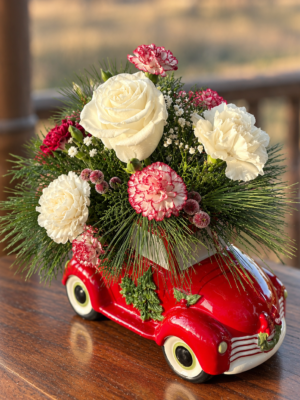 White roses, red-and-white carnations, and evergreen greenery arranged in a glossy red vintage truck Christmas container.