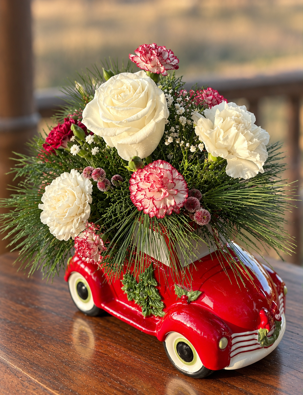 White roses, red-and-white carnations, and evergreen greenery arranged in a glossy red vintage truck Christmas container.