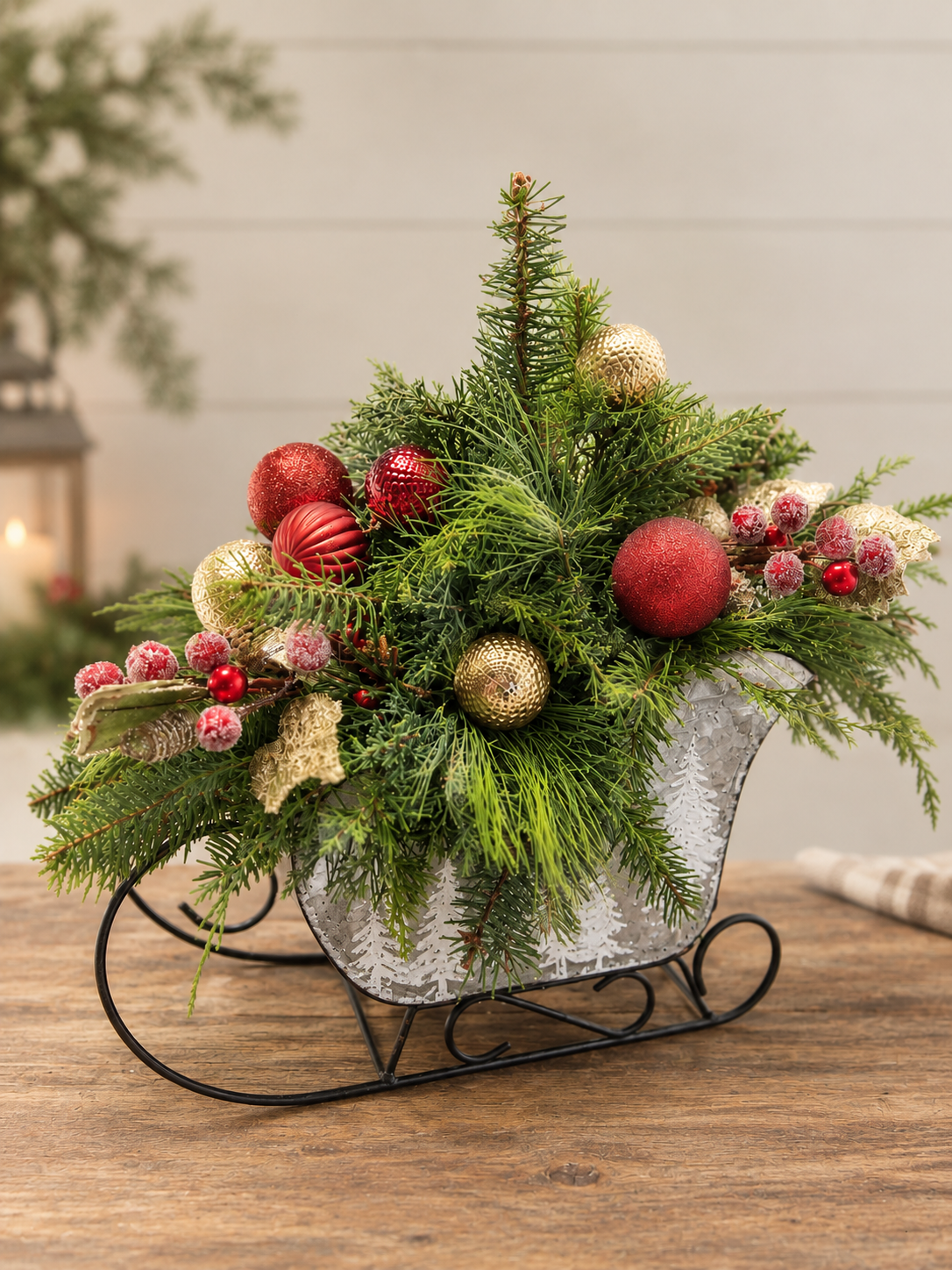 Christmas evergreen arrangement with red and gold ornaments in a galvanized metal sleigh with white tree designs